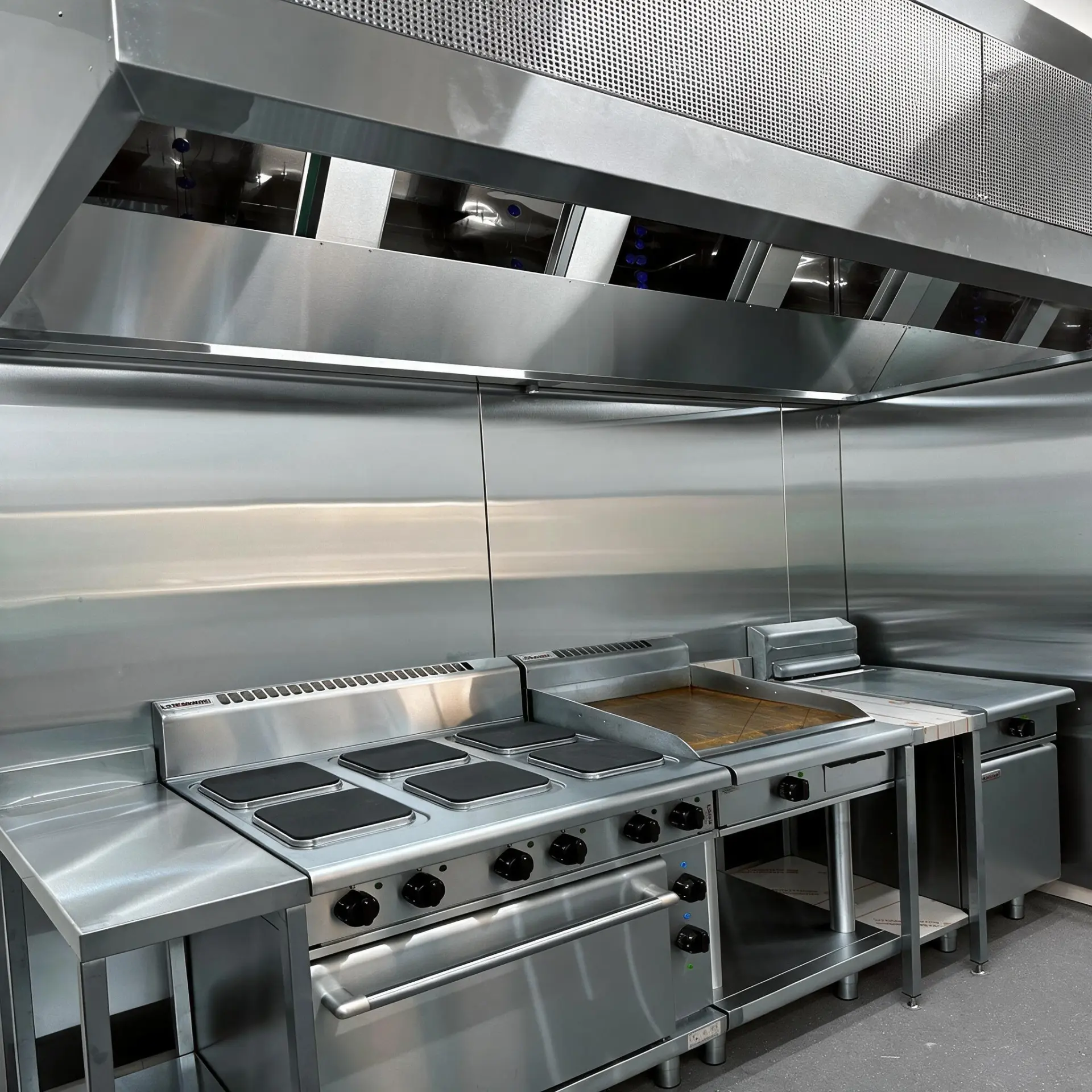 Full-width stainless exhaust canopy with makeup air plenum over an electric range and griddle line