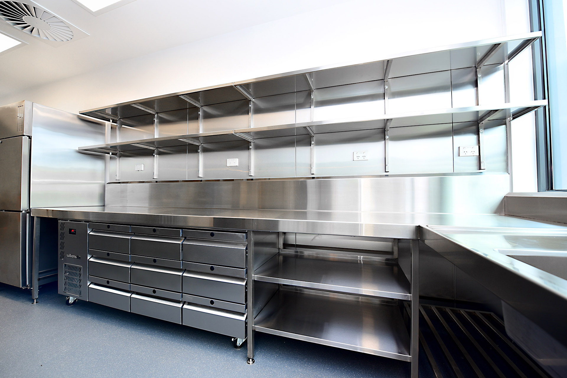 Stainless steel bench with wall shelving and refrigerated drawers