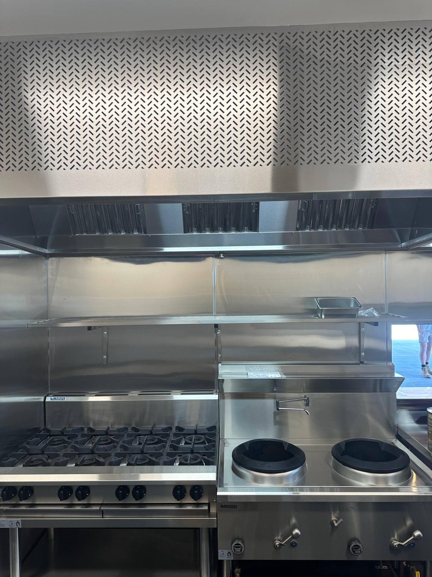 Stainless exhaust canopy with baffle filters above a commercial gas range and wok burners